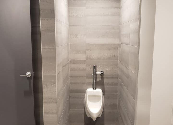 Urinal in a tiled restroom stall.